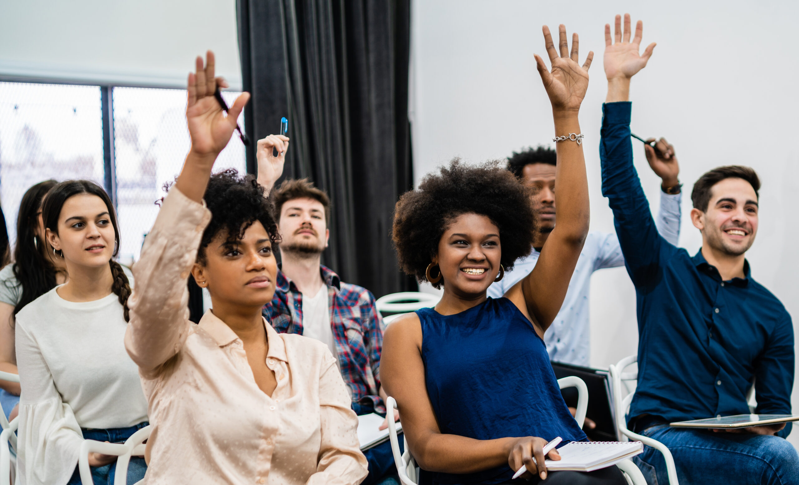 Group of young people sitting on conference together while raising their hands to ask a question. Business team meeting seminar training concept.